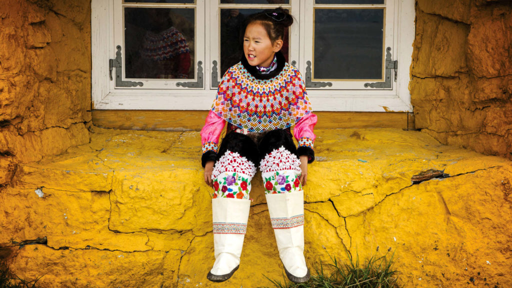 A girl from Greenland in colourful clothing greets tourists aboard Adventure Canada expedition