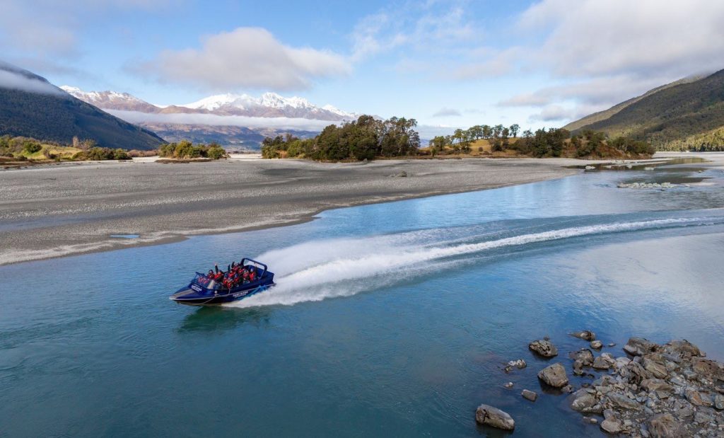 A Dart River Jet Boat zipping along the Dart River at speed with mountains in the background